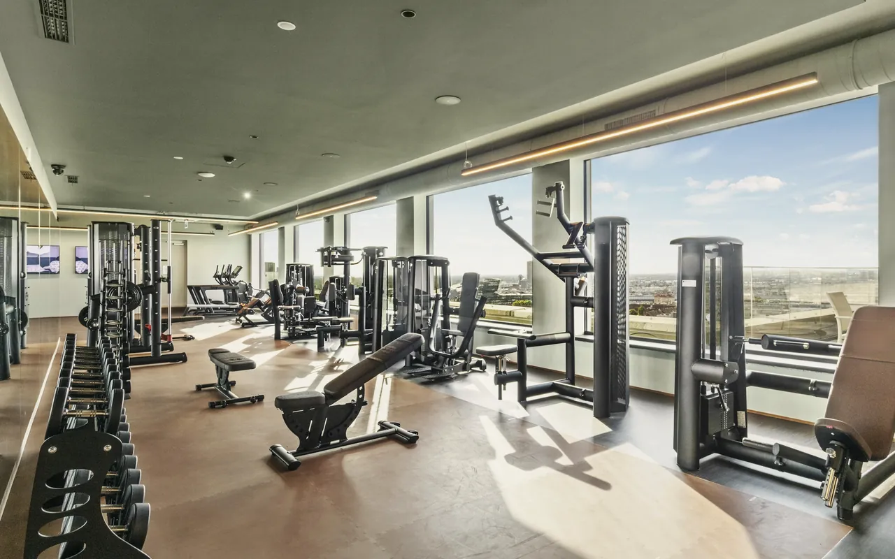 A high-floor residents’ gym in daylight: dumbbell racks, benches and strength machines by the windows