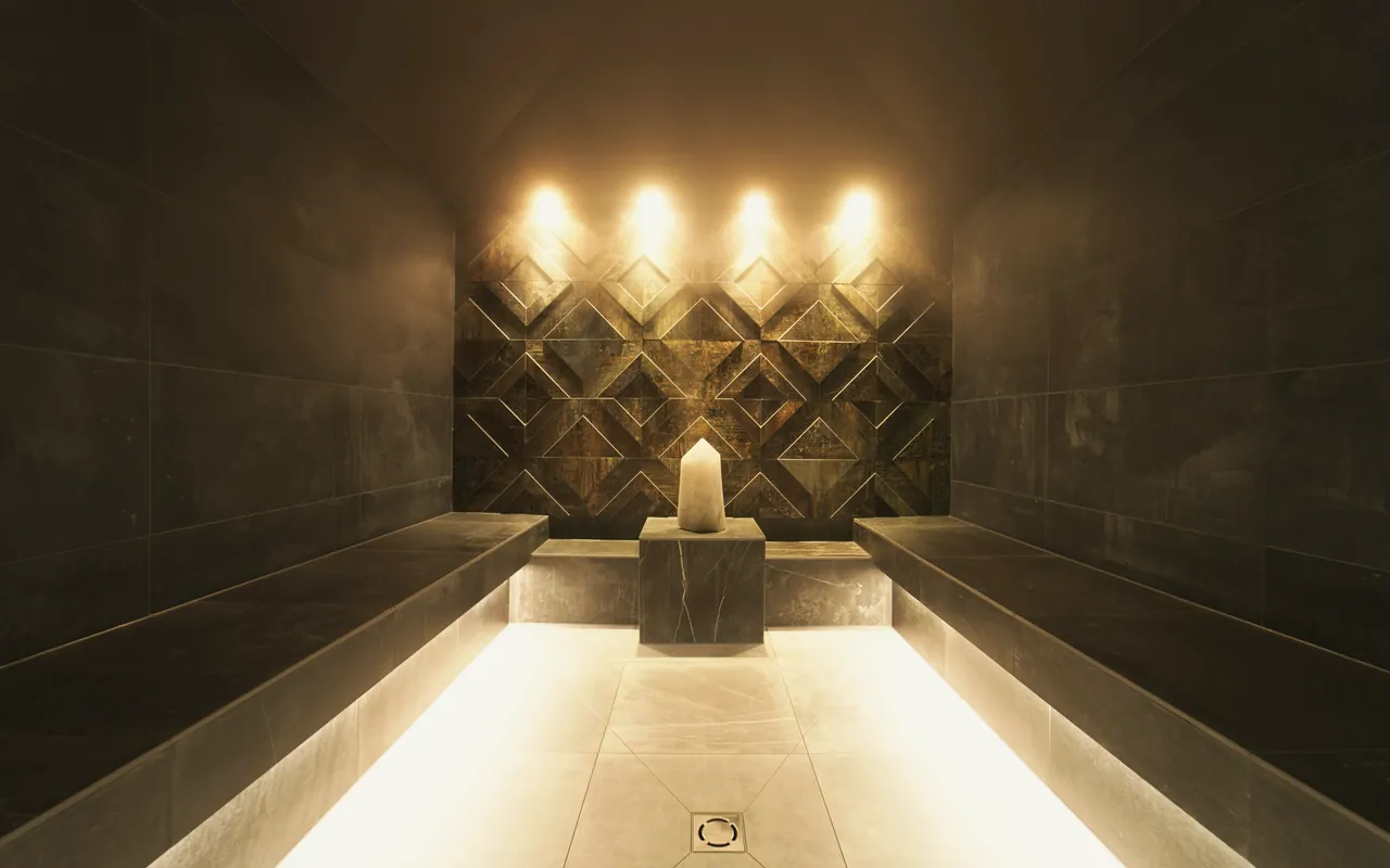 A stone-tiled steam room with two long lit benches